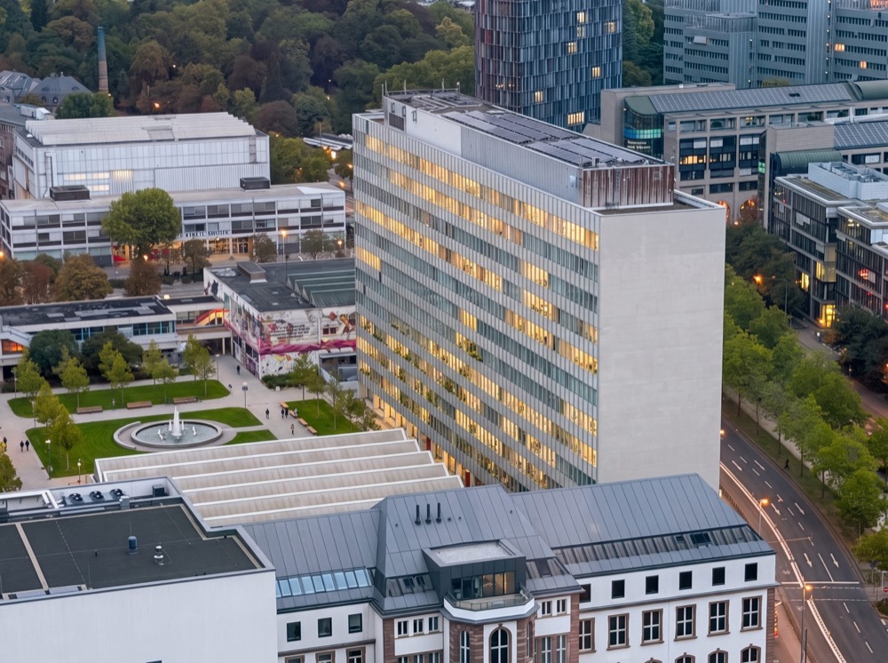 KI-generierte Luftansicht des Kulturcampus Bockenheim am Abend mit dem Juridicum und einem grünen Platz in der Mitte